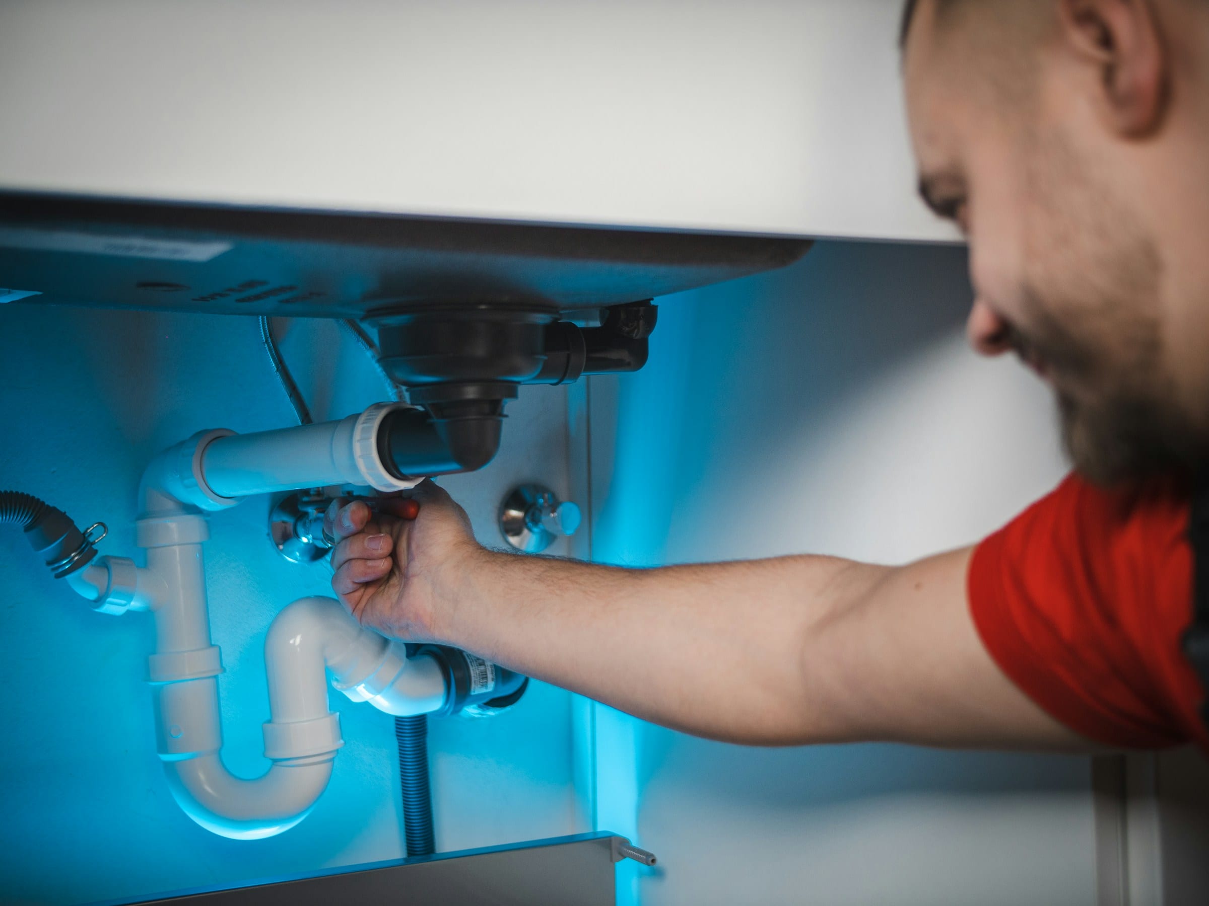 Licensed plumber working on the drain and supply lines under a kitchen sink