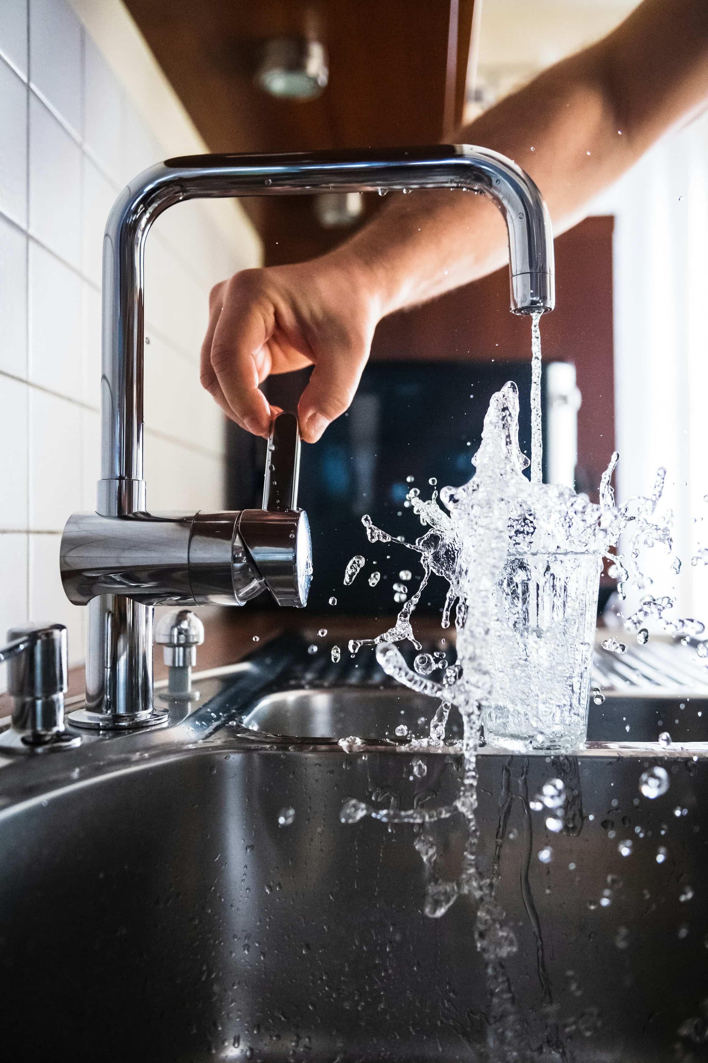 Tap water splashing into a drinking glass at a kitchen sink